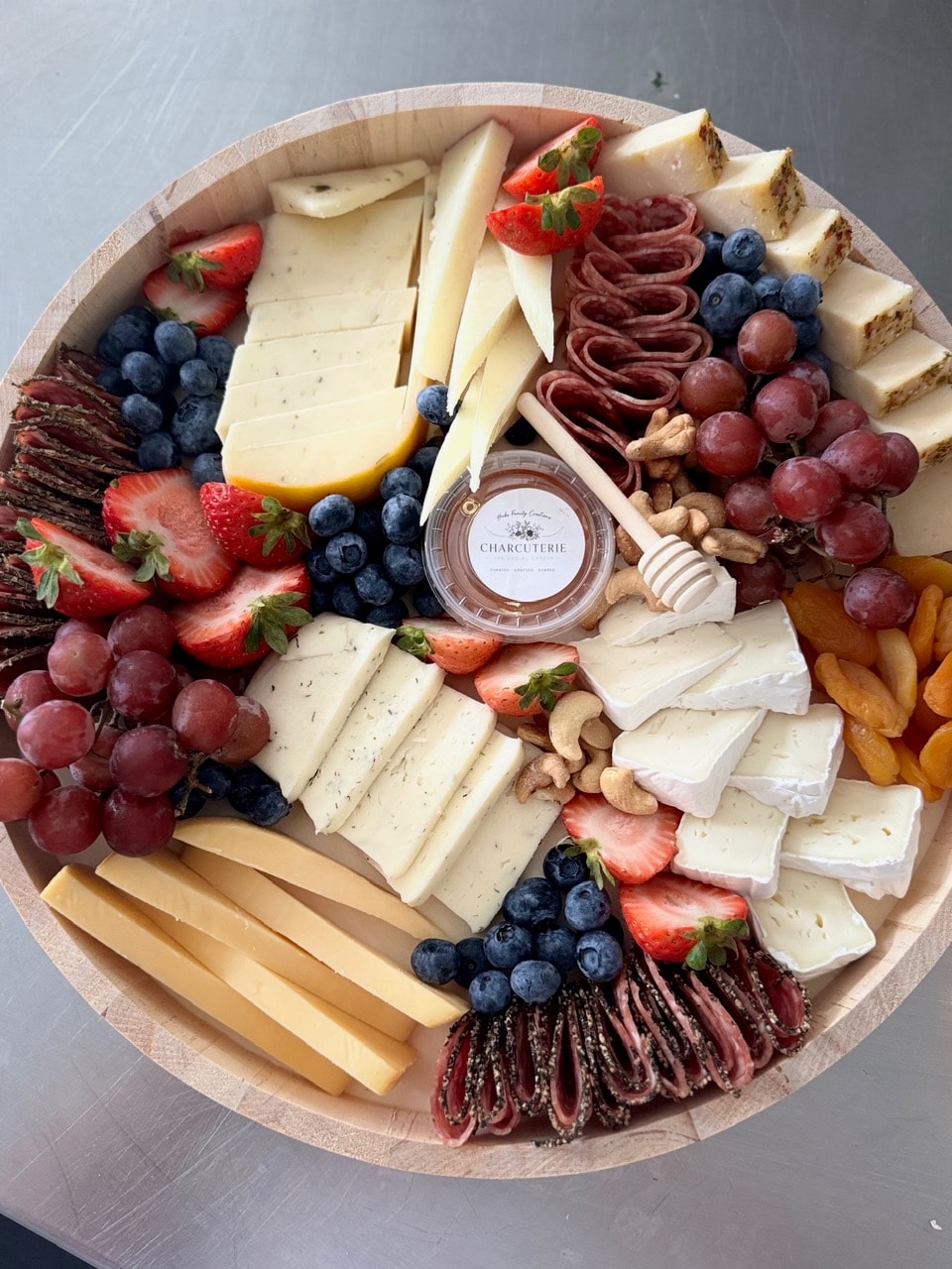 Round charcuterie board with berries, honey jar, and fresh herbs